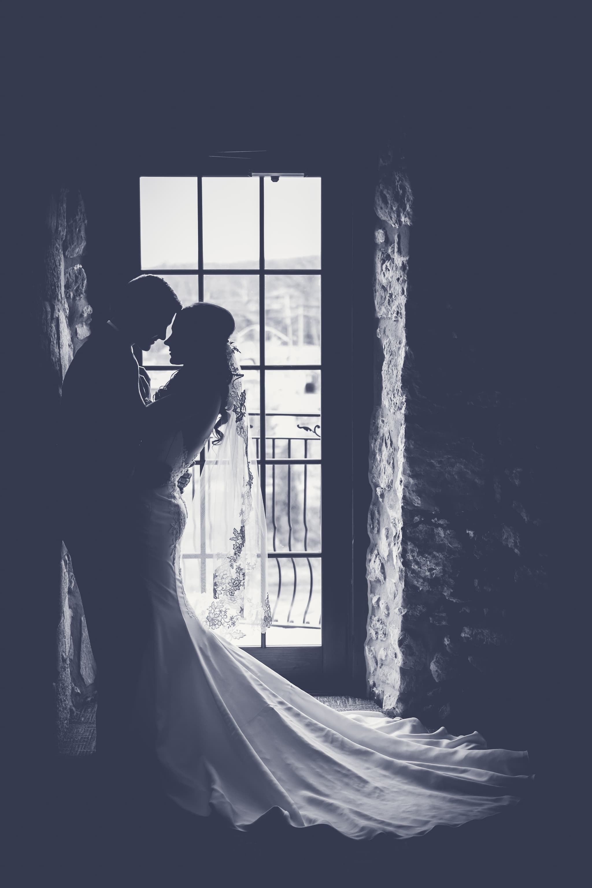 Silhouette of a bride and groom by a window, a long veil in soft backlight