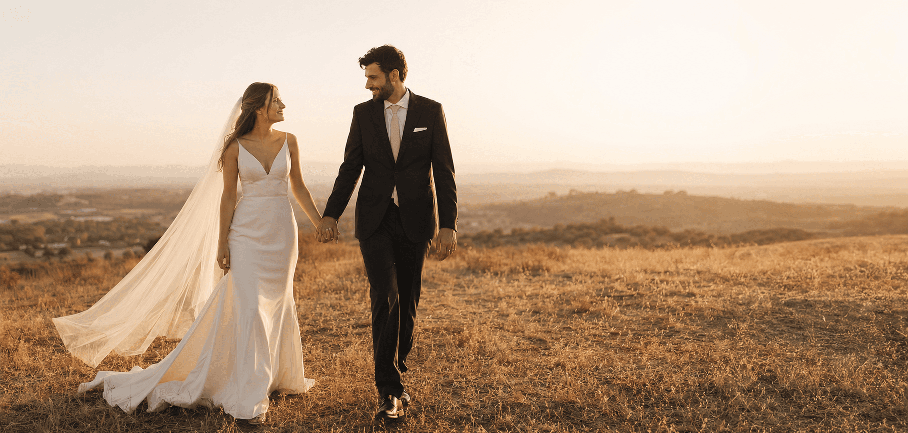 A couple walking hand in hand through a field at golden hour, the calm mood of an announcement